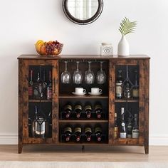 a wooden cabinet with wine glasses and bottles on it in front of a wall mounted mirror