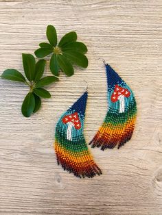 two pairs of colorful beaded earrings sitting on top of a wooden table next to green leaves