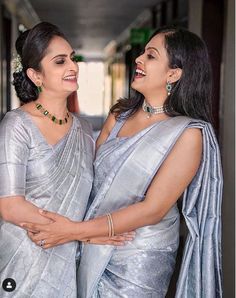 two women standing next to each other wearing silver sari and smiling at each other