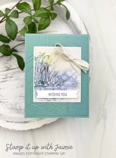 a close up of a card on a plate with a plant in the background and an envelope that says missing you