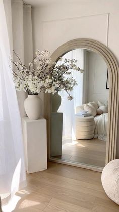 a vase filled with flowers sitting on top of a wooden floor next to a mirror