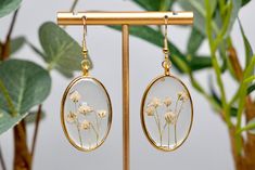 The delicate white baby's breath bundles are hand pressed, delicately arranged, and preserved in resin inside the gold, oval bezel. This elegant pair is lightweight, and can be worn all day without discomfort! They are made with hypoallergenic gold metal ear wire and crystal clear resin, allowing every detail of the baby's breath to be seen. While all pairs are assembled similarly, each flower is unique, making every pair one of a kind! Due to the products handmade nature, please understand that Delicate Oval Pressed Flower Jewelry, Delicate Oval Jewelry With Pressed Flowers, White Resin Earrings With Pressed Flowers, Gold Teardrop Flower Earrings With Pressed Flowers, White Pressed Flower Drop Earrings, White Pressed Flowers Drop Earrings, White Drop Earrings With Pressed Flowers, Gold Adjustable Birth Flower Earrings, Adjustable Gold Birth Flower Earrings