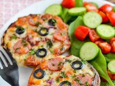 two small pizzas on a white plate with vegetables and a fork next to it