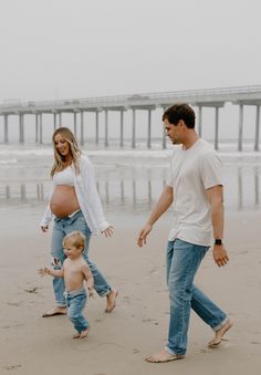 a man and woman walking on the beach with a baby in their lap while holding hands