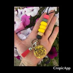 a person's hand holding two different colored beads and a keychain with the word miss smith on it