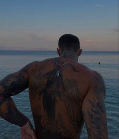 a man with tattoos on his back standing in front of the ocean