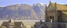 an old building with mountains in the background and people standing on it's roof