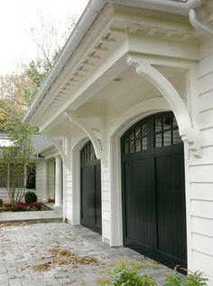 a white house with black garage doors and brick walkway