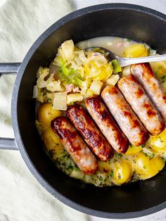 sausages and potatoes in a skillet with a spoon resting on the side, ready to be eaten