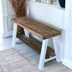 a wooden bench sitting in front of a window next to a vase with dried flowers