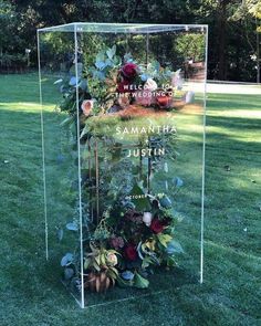 a clear acrylic sign with flowers and greenery on the grass in front of it