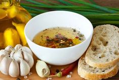 a bowl of soup next to bread and garlic on a cutting board