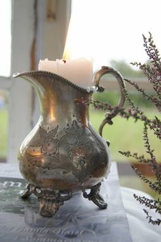 a silver vase sitting on top of a table with a lit candle in the middle