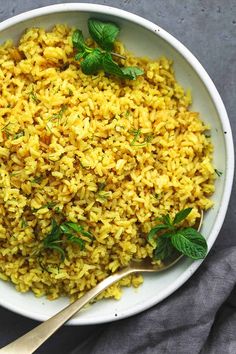 a white bowl filled with yellow rice and garnished with fresh mint on top