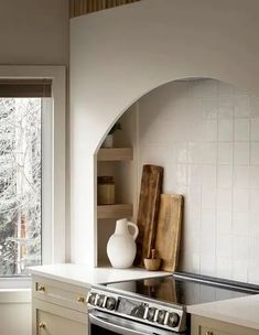 a stove top oven sitting inside of a kitchen next to a wooden cutting board and window