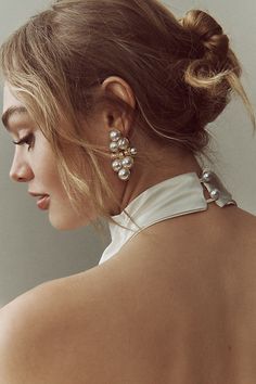 a woman with her back turned to the side wearing large earrings and a white blouse