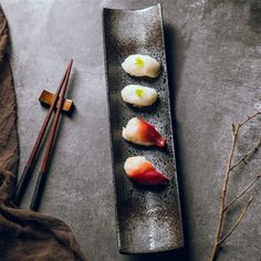 three sushi on a black plate with chopsticks next to it and a brown cloth