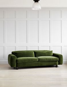 a green couch sitting on top of a hard wood floor next to a white wall