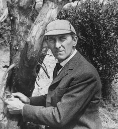 an old photo of a man in a suit and hat sitting next to a tree