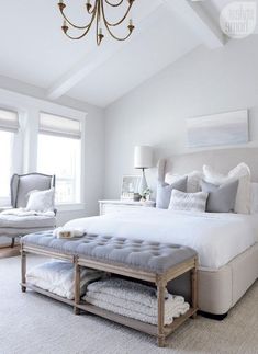 a large white bed sitting in a bedroom under a chandelier next to two windows