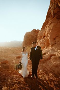 a bride and groom walking through the desert