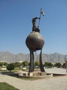 a statue of a man holding a flag on top of a stone ball in the middle of a park