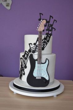 a white and black guitar cake with music notes on the top, sitting on a table in front of a purple wall