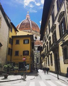 people are walking down the street in an old european city with tall buildings and a dome