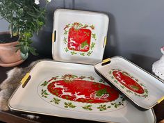 three trays with christmas designs on them sitting on a table next to a potted plant