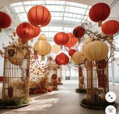 many red and white lanterns hanging from the ceiling in an indoor area with trees, shrubs and flowers