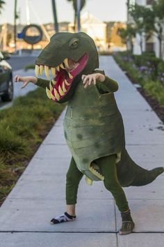 a child in a dinosaur costume on the sidewalk