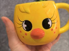 a close up of a person holding a yellow cup with a bird face on it