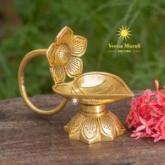 a gold colored metal vase with flowers on the table next to it and a red flower