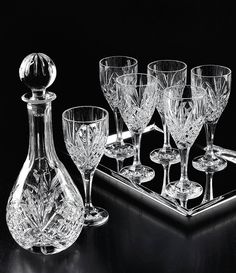 an assortment of crystal wine glasses and decanter on a black table with a reflective surface