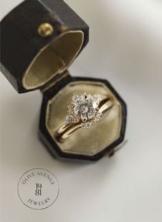 an open ring box with a diamond in it on a white surface, next to a black and gold ring