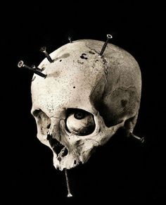 a black and white photo of a human skull with nails on it's head