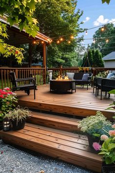 Wooden deck with string lights, cozy seating around a fire pit, and lush green surroundings featuring various colorful plants and flowers. Backyard Deck Aesthetic, Fire Pits On Wooden Decks, Covered Patio And Deck Combo, Tiny Home Deck Ideas, Basic Deck Ideas, Cozy Deck Ideas Outdoor, Creative Deck Design, Back Deck Furniture Ideas, Deck Oasis Ideas