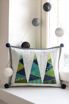 a decorative pillow with christmas trees on it sitting next to a window in a room