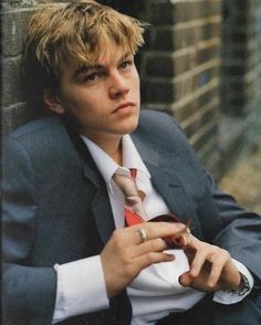 a young man wearing a suit and tie leaning against a brick wall with his hands on his hips