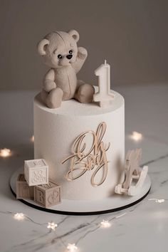 a white cake with a teddy bear on top and candles in the shape of letters