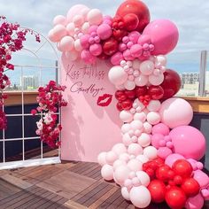 pink and red balloons are hanging on the side of a wall with a sign that says kiss my lips goodbye