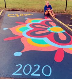 a person sitting on the ground in front of a colorful painted parking lot with flowers