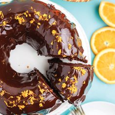 a chocolate bunt cake with orange slices around it on a white plate and blue background