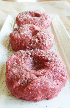 three hamburger patties sitting on top of a white plate covered in seasoning sprinkles