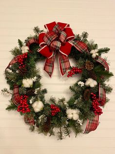 a christmas wreath hanging on the wall with red and white bows, berries, pine cones and cotton balls