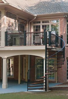 a spiral staircase in front of a large brick house with glass doors and windows on the second floor