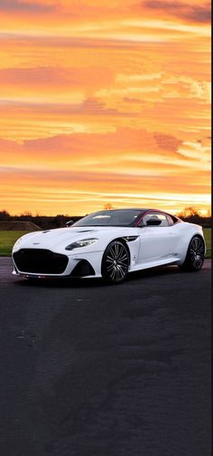 a white sports car parked on the side of a road in front of a sunset