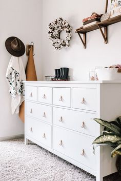 a white dresser sitting on top of a carpeted floor next to a potted plant