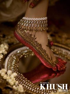 a woman's feet in gold and red shoes with jewels on the bottom, surrounded by flowers