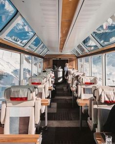 the inside of a train car with tables and chairs on each side, looking out at snow covered mountains